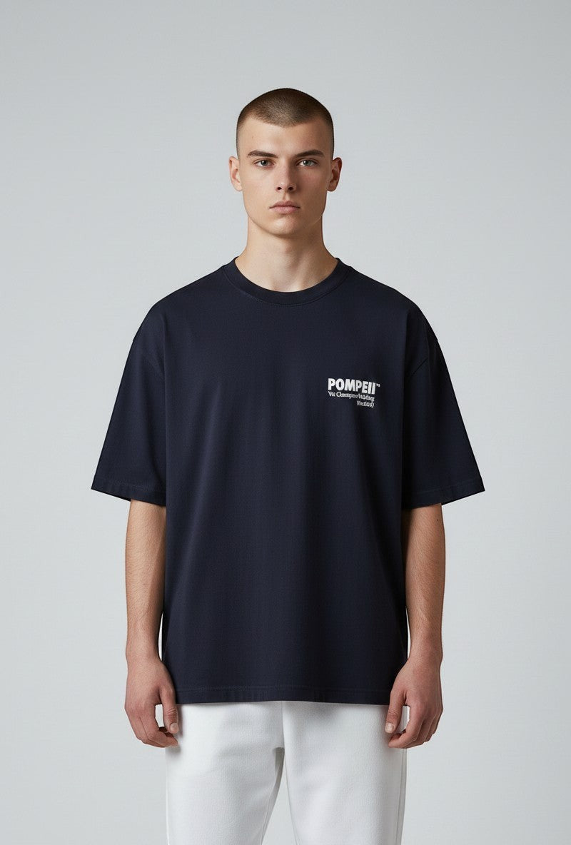 Modello indossa T-shirt blu navy ULTIMATAGLIA.COM Pompeii in cotone pesante con logo bianco sul petto e fit boxy.