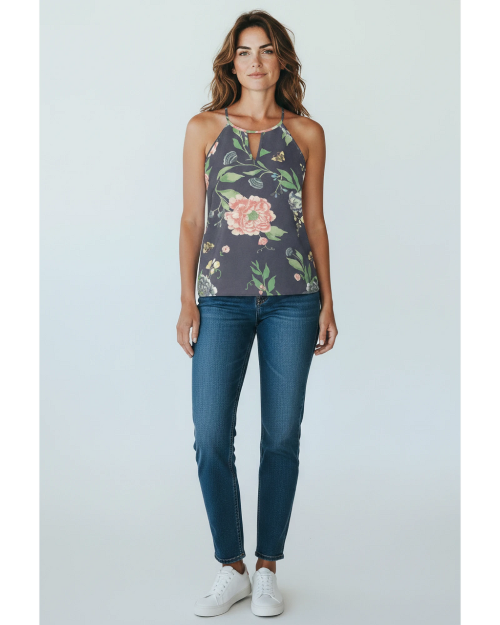 Modella indossa top smanicato ULTIMATAGLIA.COM con stampa floreale, scollo a goccia e jeans blu su sfondo neutro