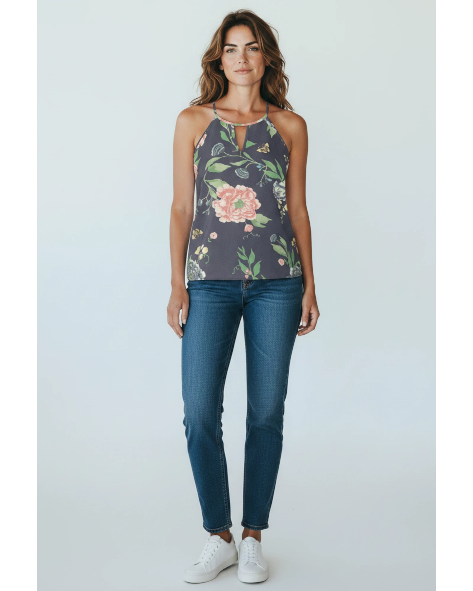Modella indossa top smanicato ULTIMATAGLIA.COM con stampa floreale, scollo a goccia e jeans blu su sfondo neutro